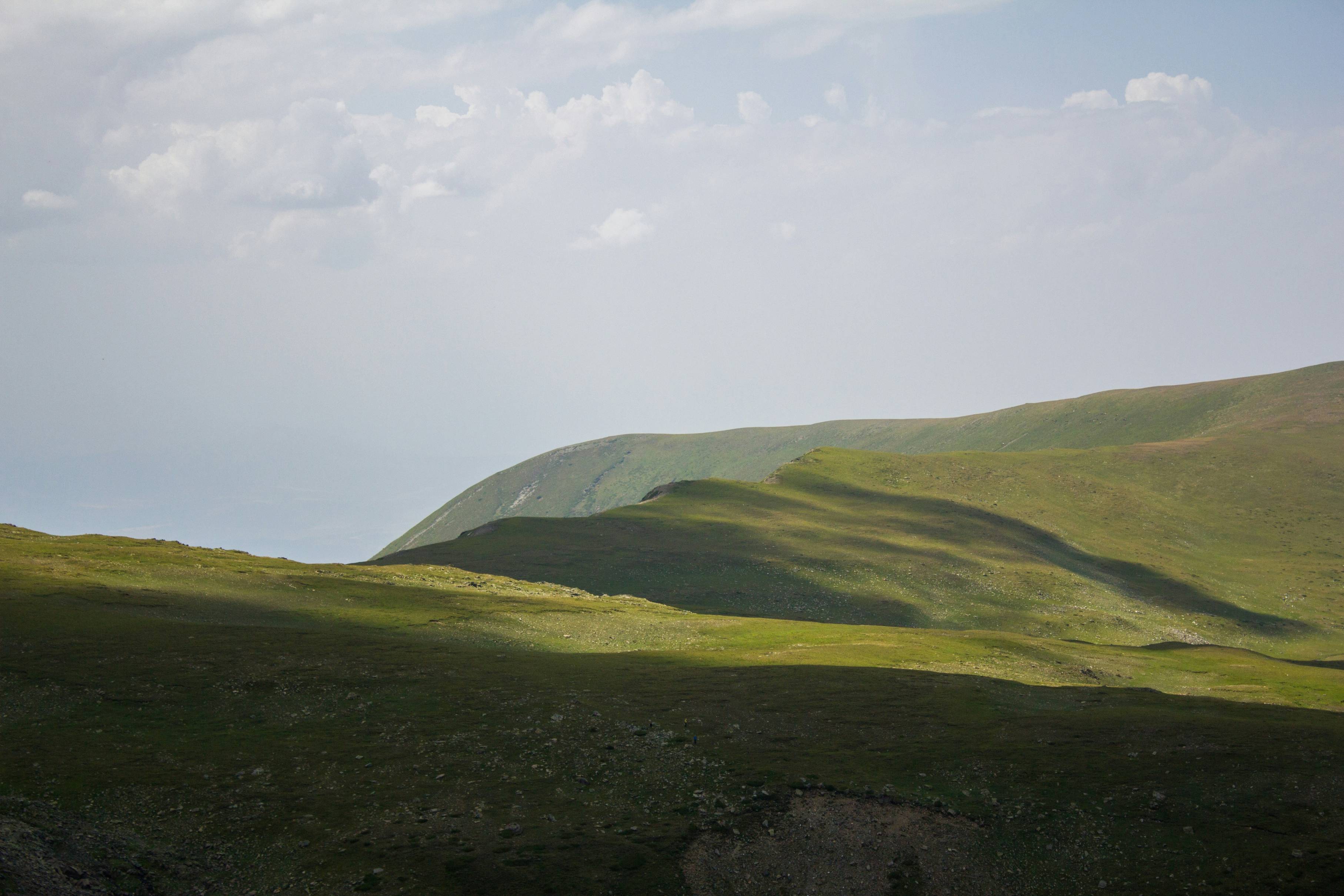 a grassy hill with a few clouds in the sky